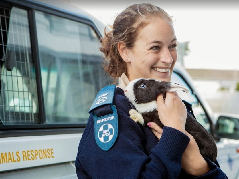 SPCA inspector smiling while holding a rescued rabbit beside a response vehicle